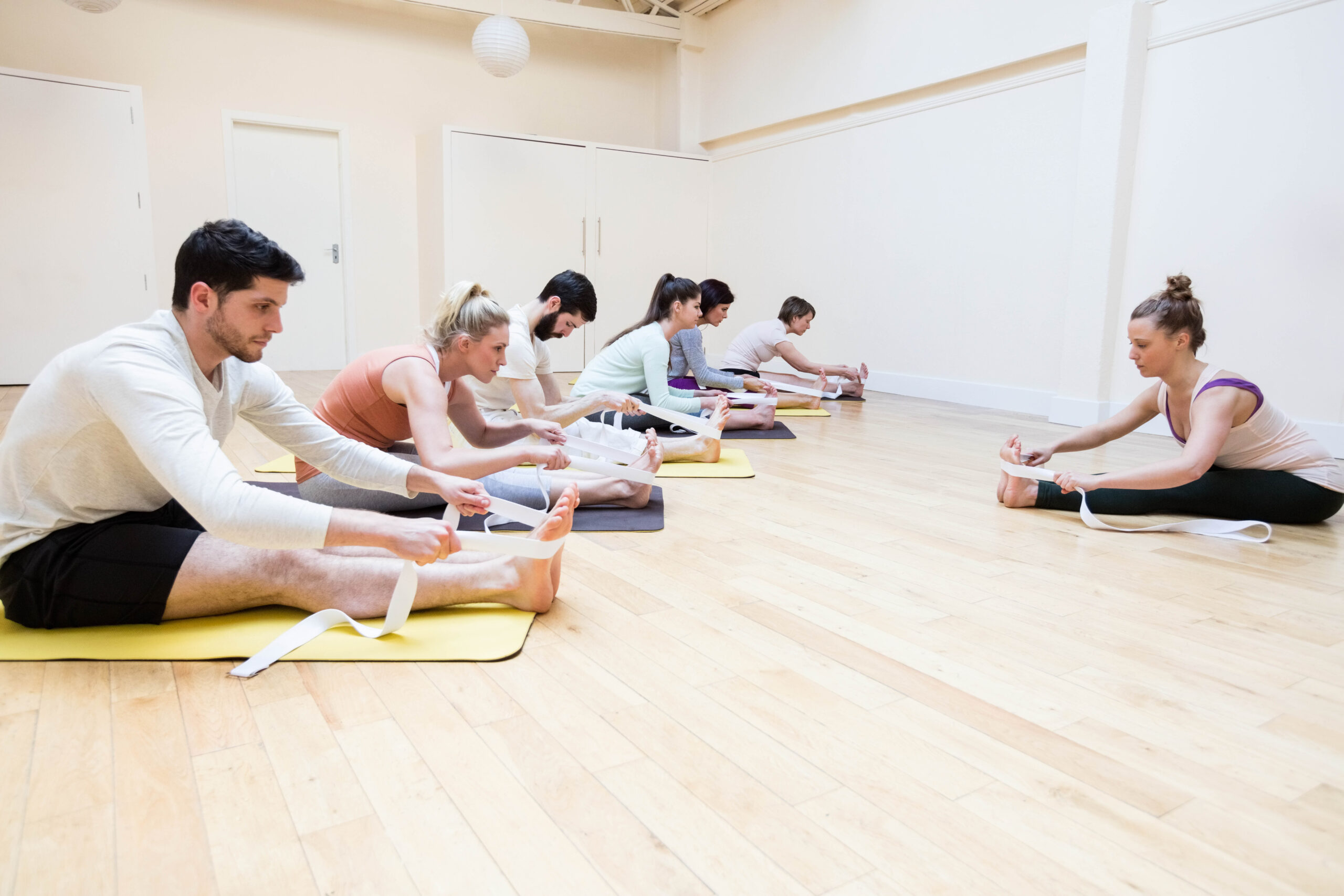 Trainer assisting group of people with stretching exercise in the fitness studio